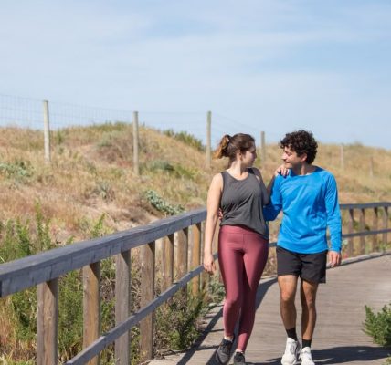 A couple in activewear strolling together on a sunny boardwalk in a natural setting.