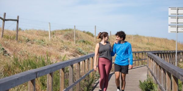 A couple in activewear strolling together on a sunny boardwalk in a natural setting.