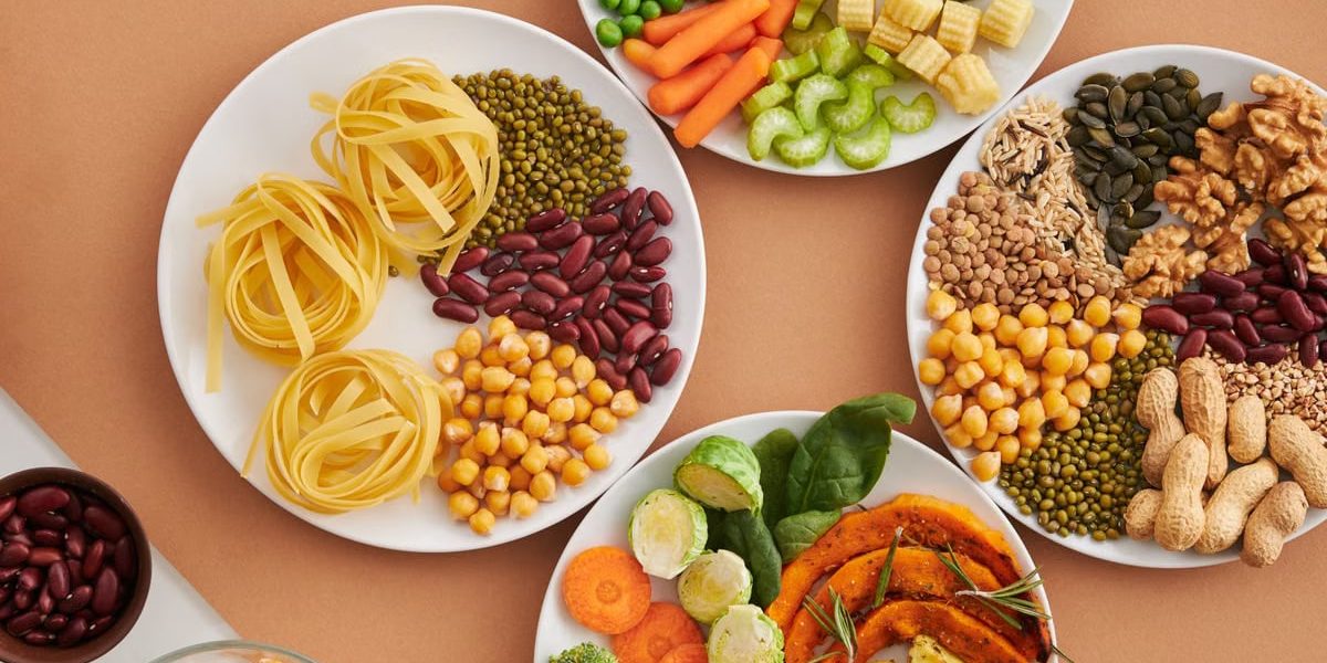A vibrant mix of legumes, vegetables, nuts, and pasta arranged on white plates showcasing a balanced, healthy diet.