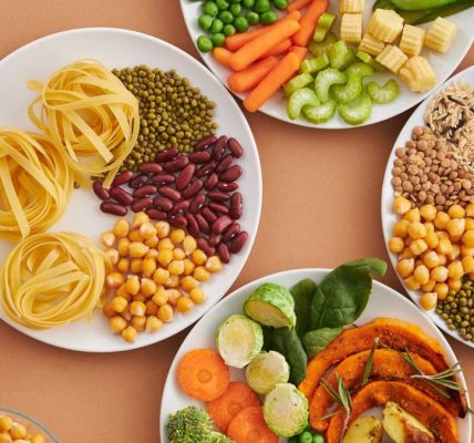 A vibrant mix of legumes, vegetables, nuts, and pasta arranged on white plates showcasing a balanced, healthy diet.
